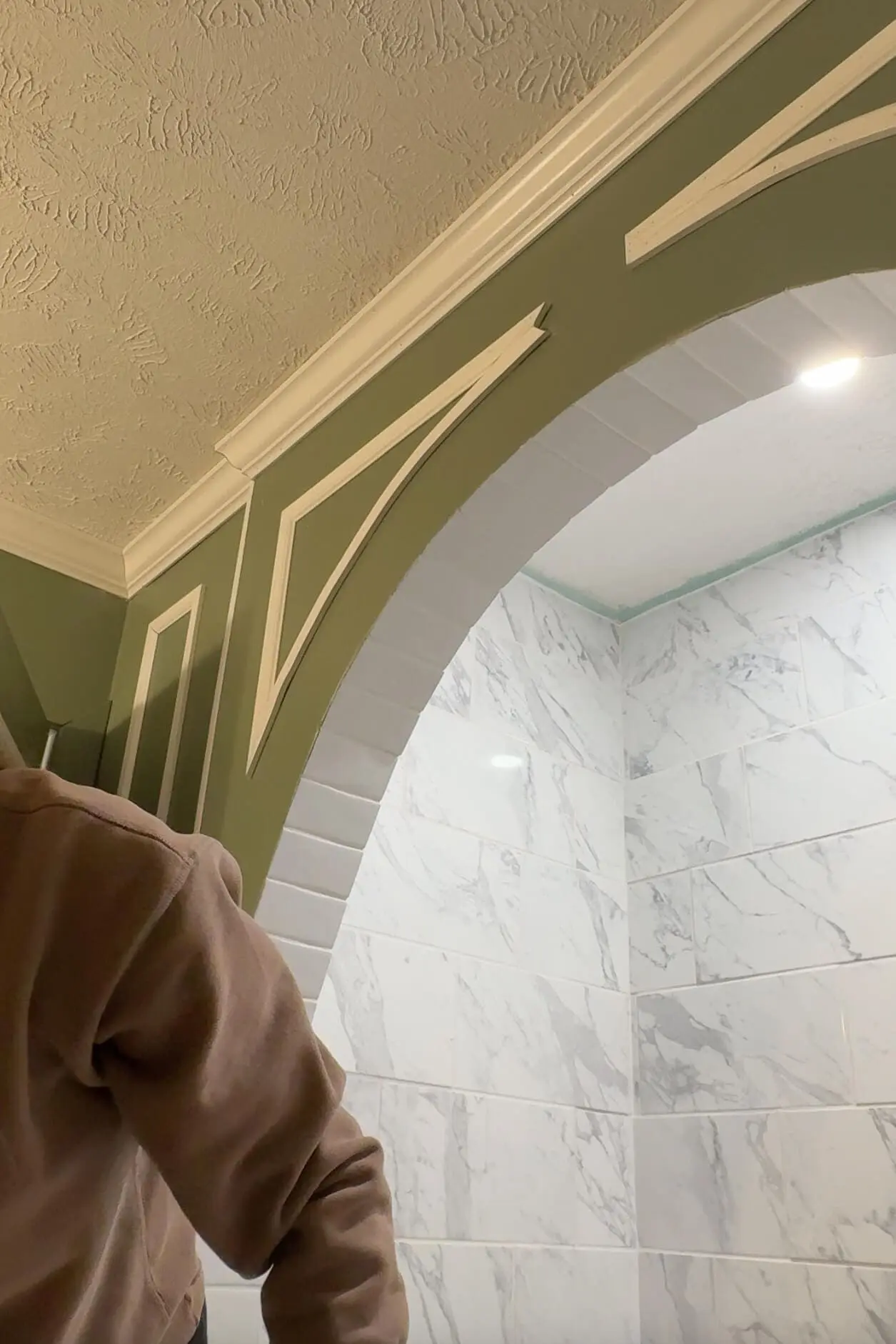 View of a beautifully completed green archway with white curved trim details, complemented by crown molding and glossy marble-patterned tiles in the adjacent room. A clean and elegant DIY transformation.